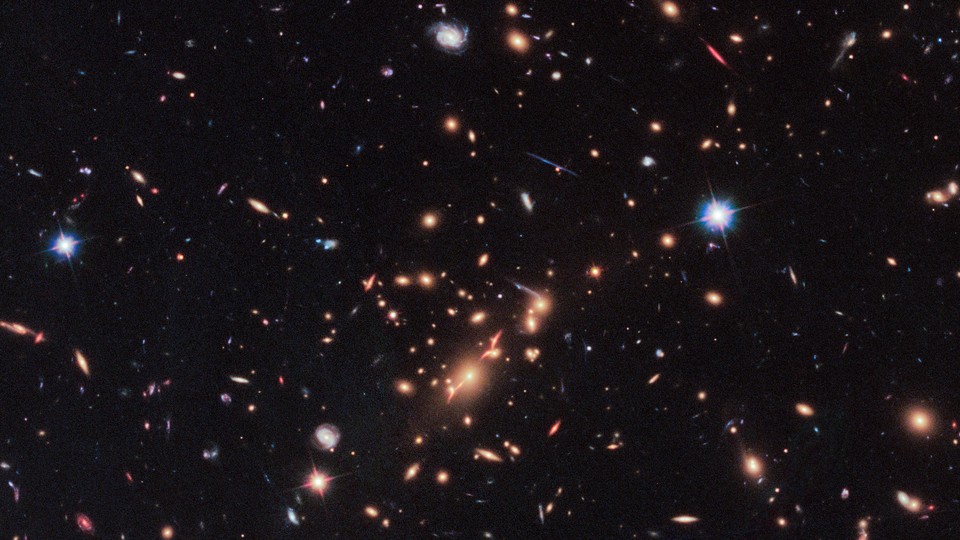  A Hubble Telescope image that includes a red, disk-shaped galaxy seen through a gravitational lens in the upper right corner.