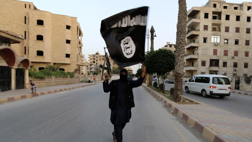 A man walks down a street holding an ISIS flag and a gun in Raqqa.