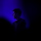 Photograph of Sam Altman in a dark room, his shoulders and face illuminated by a blue light