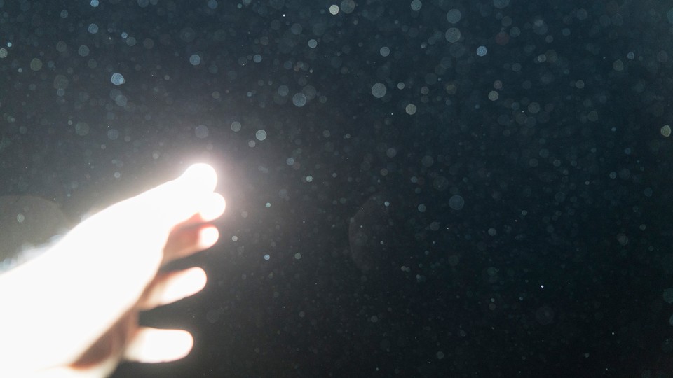 a brightly lit hand reaching out to the dark sky, the lens smudged with rain drops