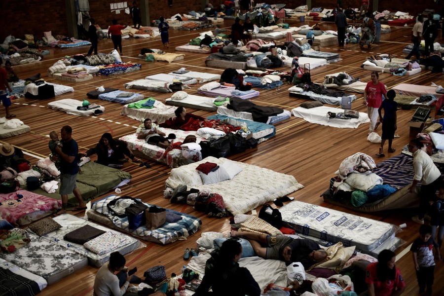 People rest on mattresses and cots set up inside a gymnasium.