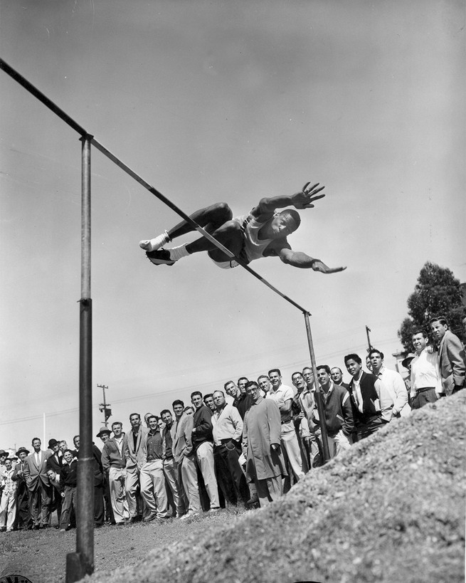 black and white photo of bill russell doing a high jump