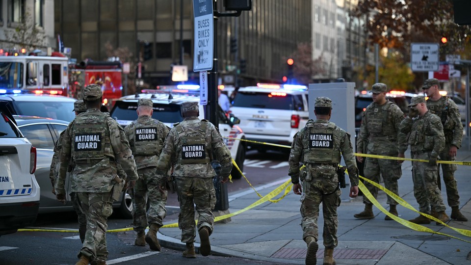 National Guardsmen in camouflage uniforms walk down a street in Washington, D.C., with yellow tape.