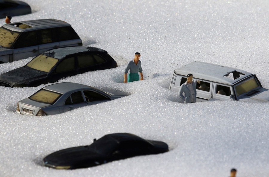 Tiny figurines of people and cars are seen in snow.