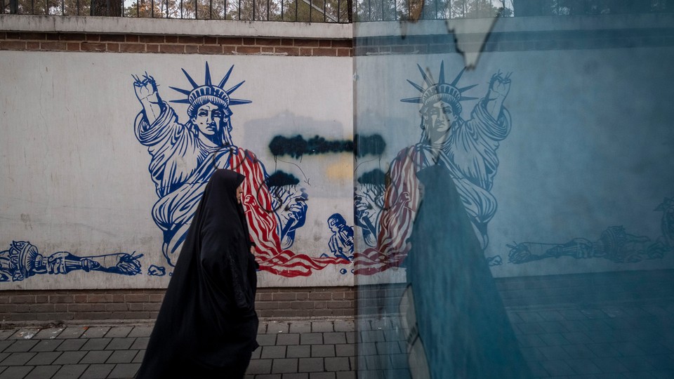 Photograph of a woman wearing a black body covering walking past graffiti of a defaced Statue of Liberty