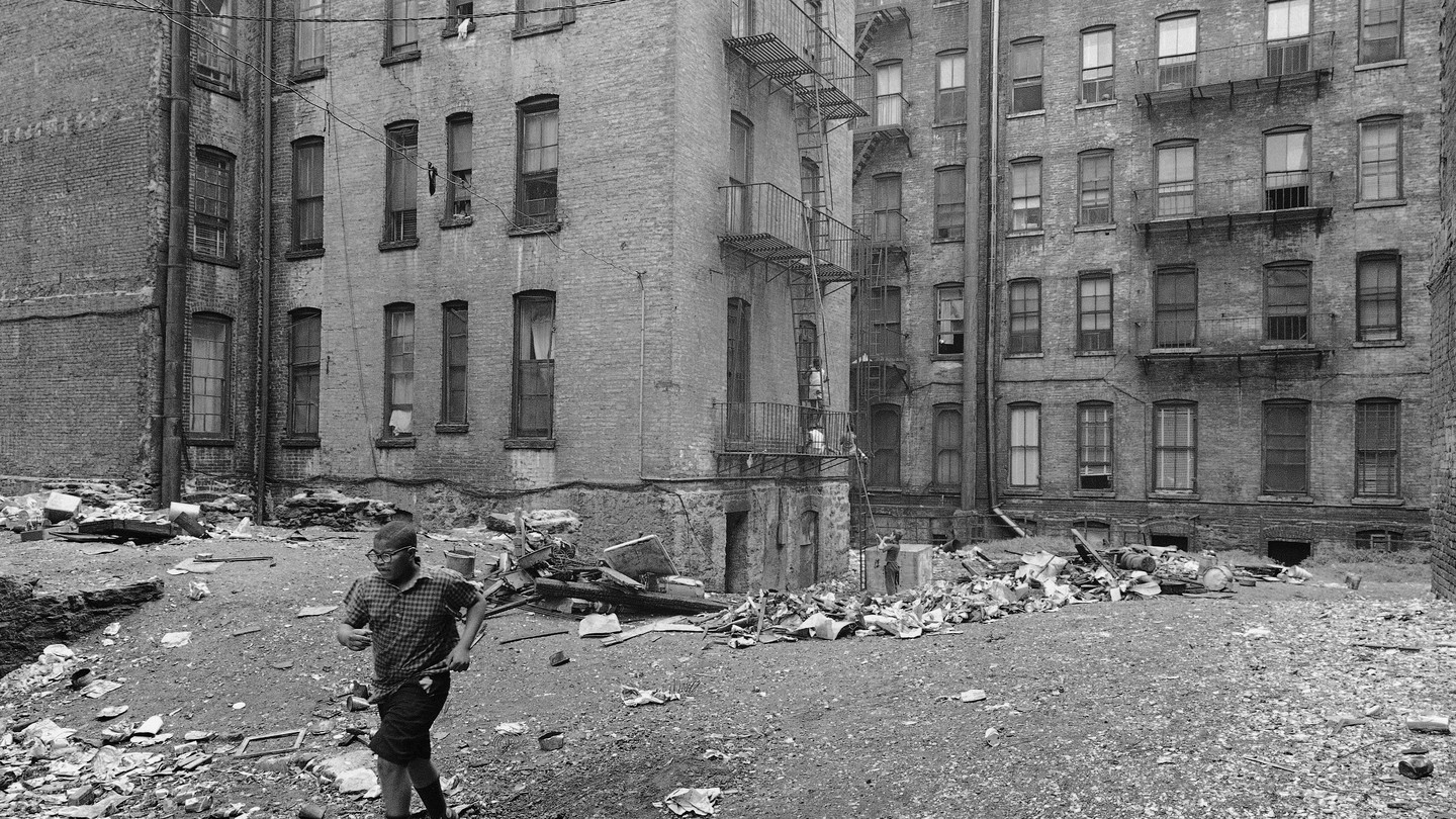 A black-and-white photo of a child running through New York City tenements
