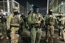 Photograph of about a dozen agents with their faces covered, dressed in green camouflage or tactical gear