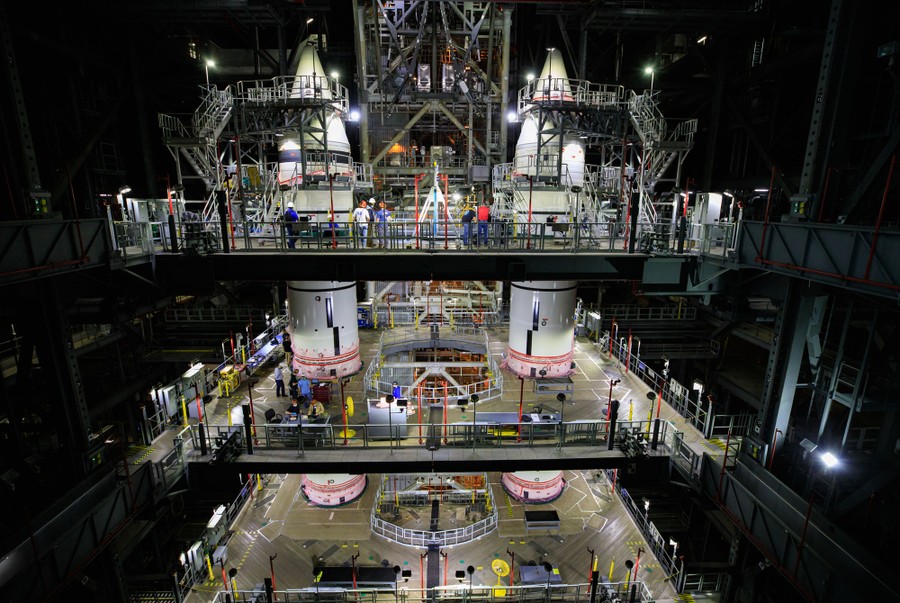 A view of several decks surrounding two tall rocket boosters, and about a dozen workers in various places.