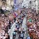 Crowds on either side of a city street cheer racing cyclists as they ride past.