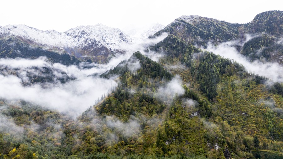 Mountains are cloaked in misty clouds, some capped with early snow.