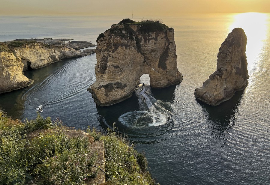 A man rides a jet ski under an arch in a rock formation just offshore.