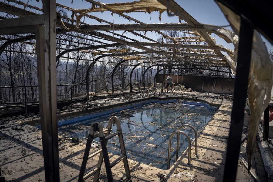 A person walks near a swimming pool under the burned shell of a pool cover.