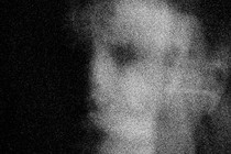 A blurred black-and-white photo of a young man's face.