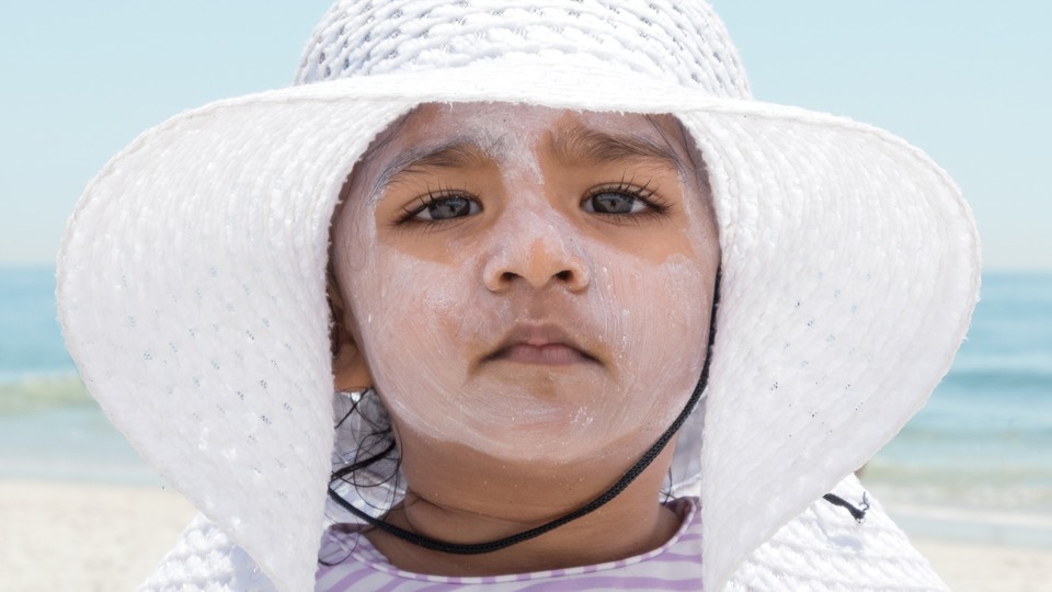 A child in a white hat with lots of sunscreen on her face
