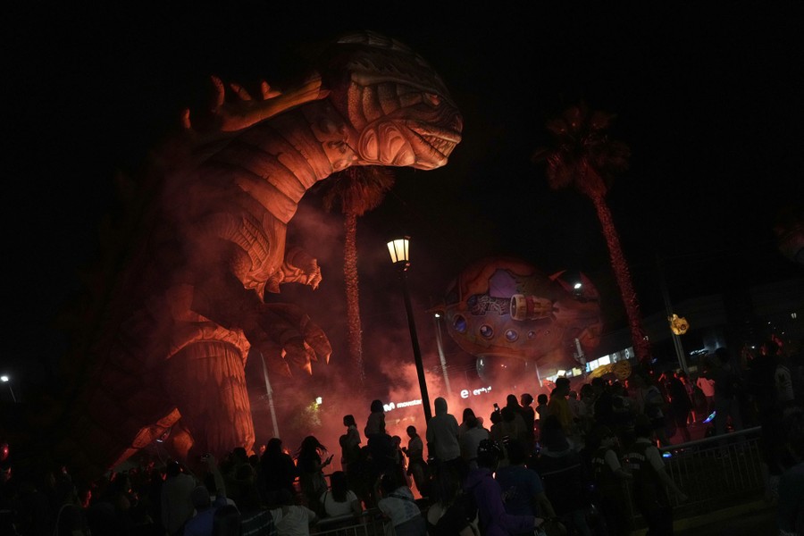 A crowd watches a parade featuring a huge inflatable dinosaur.