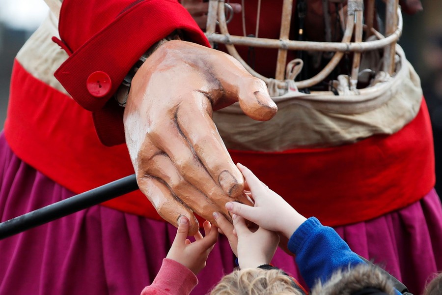 Several children reach up to touch the hand of a giant puppet.