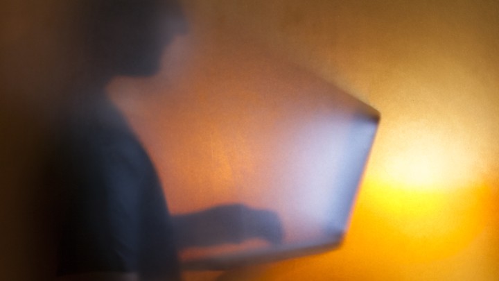 The silhouette of a man looking at a bright computer screen