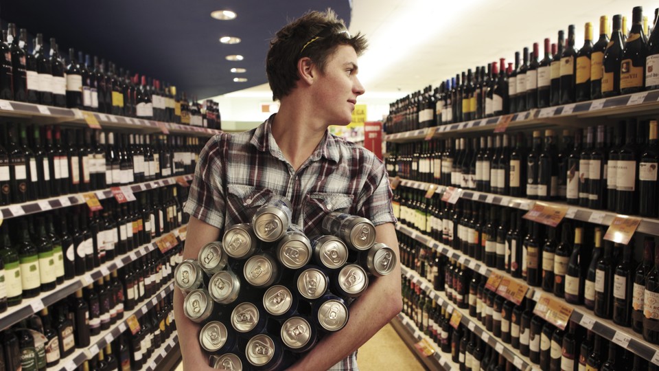 A young man walks down a wine aisle holding many cans.