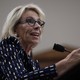 Betsy DeVos gestures while sitting at a microphone