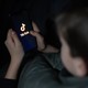 A 12-year-old boy looks at a smartphone screen displaying the TikTok logo