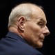 Former White House Chief of Staff John Kelly is seen in profile. The background behind him is black and he's wearing a navy suit.