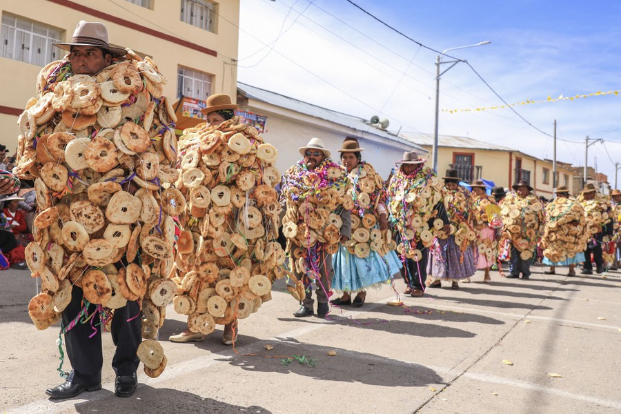 About a dozen people march in a parade, each wearing many small pieces of bread and other food hanging across their bodies.