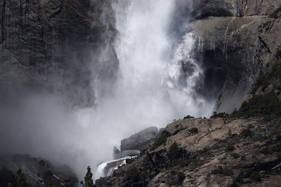 Two people are silhouetted in the distance against a huge waterfall