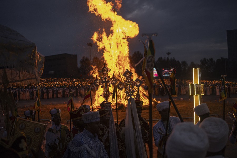 People carry crosses and dress in religious garments while standing around a large bonfire.