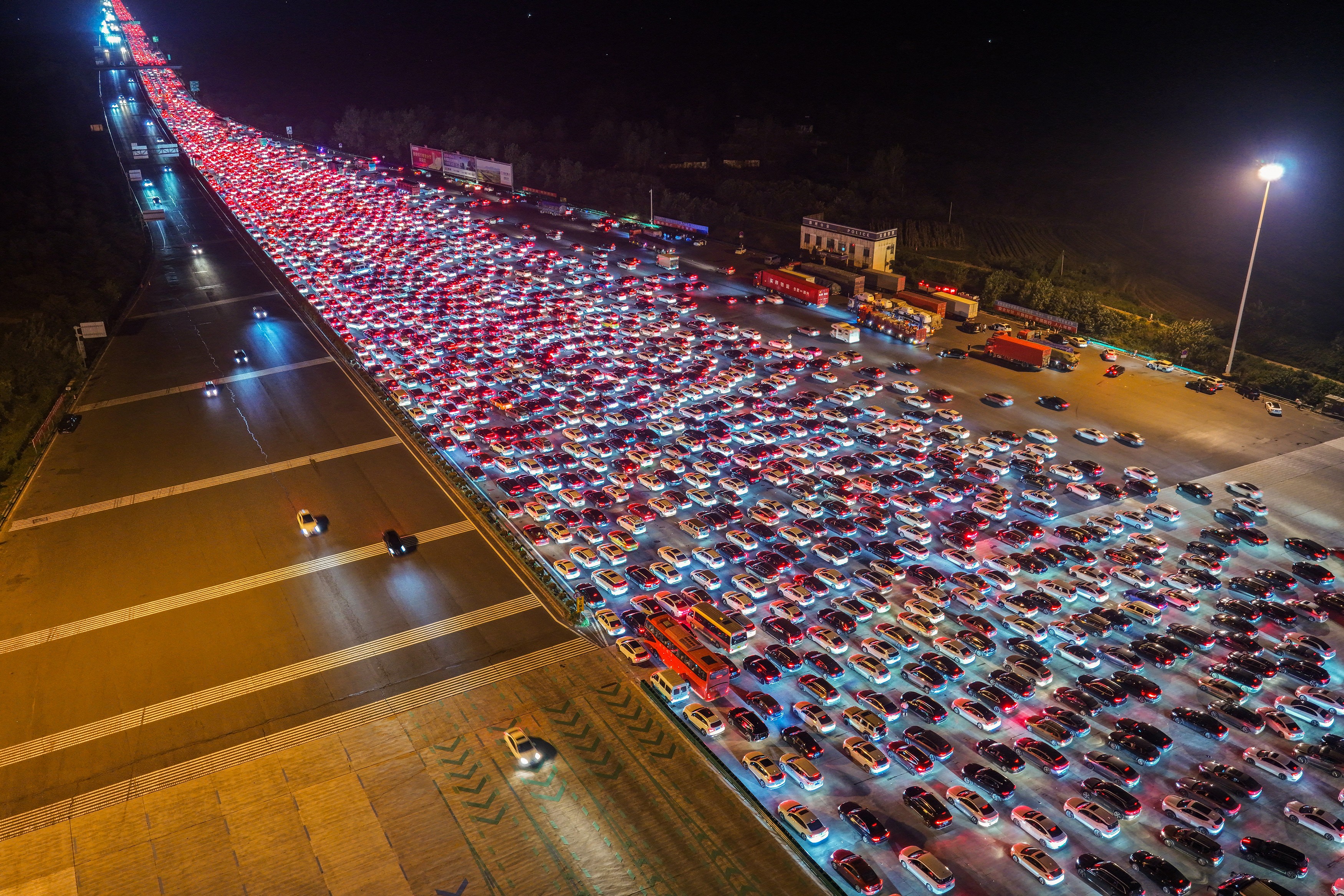 Hundreds of cars merge from several dozen lanes down to just a few, seen from above, a sea of red brake lights.