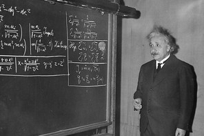 A black and white photograph of Albert Einstein in front of a blackboard