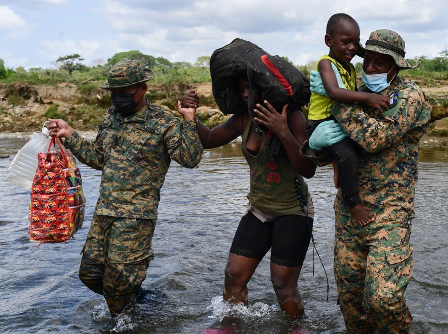 Soldiers help a woman and a child across a shallow part of a river.