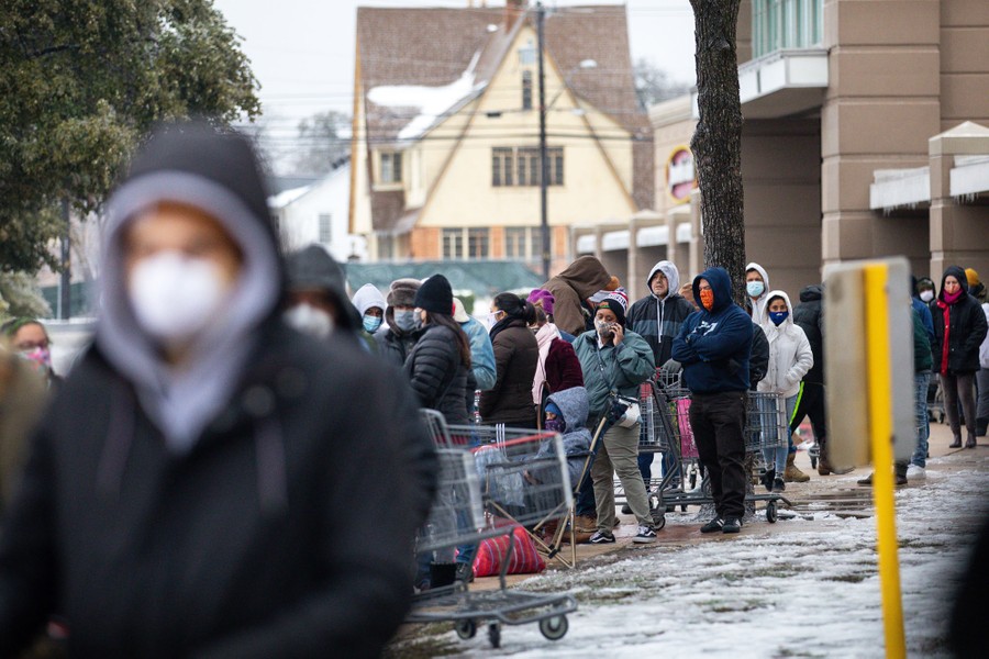 A long line of people stand in cold weather outside a grocery store.
