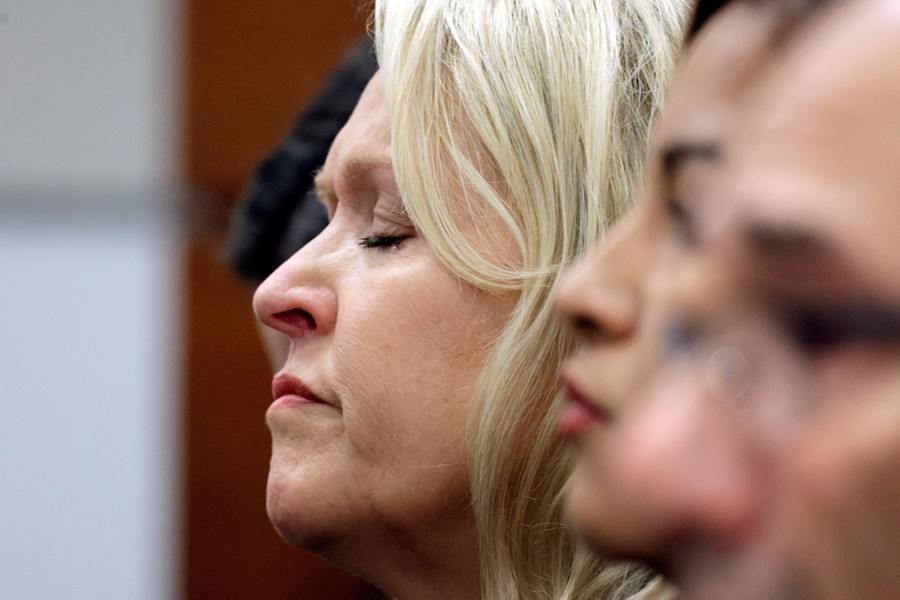 A woman closes her eyes, seated beside others in a courtroom.
