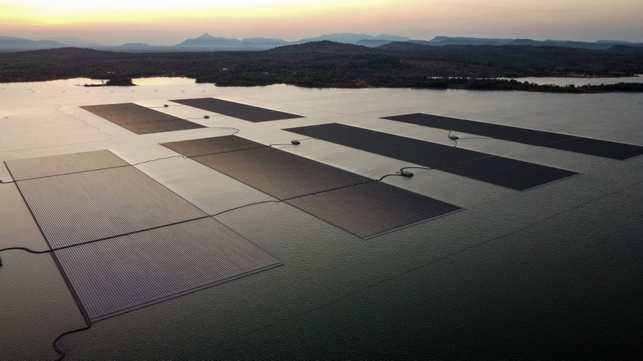 An aerial view of multiple large arrays of solar panels, floating in a bay