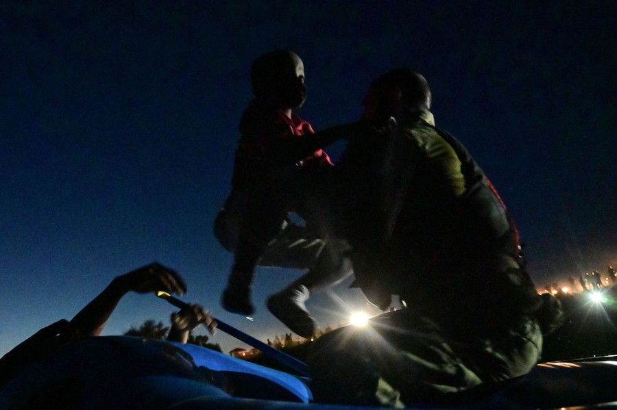 A border patrol officer lifts a child into a boat.