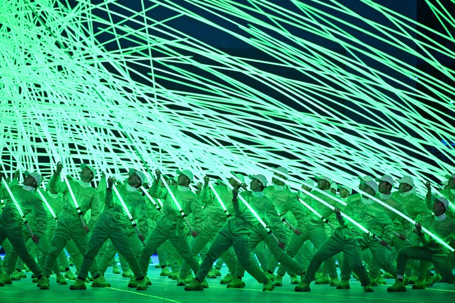 Dozens of performers hold up long glowing green tubes.
