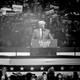 A black-and-white photo of Donald Trump standing at a podium, speaking to a crowd at Madison Square Garden.
