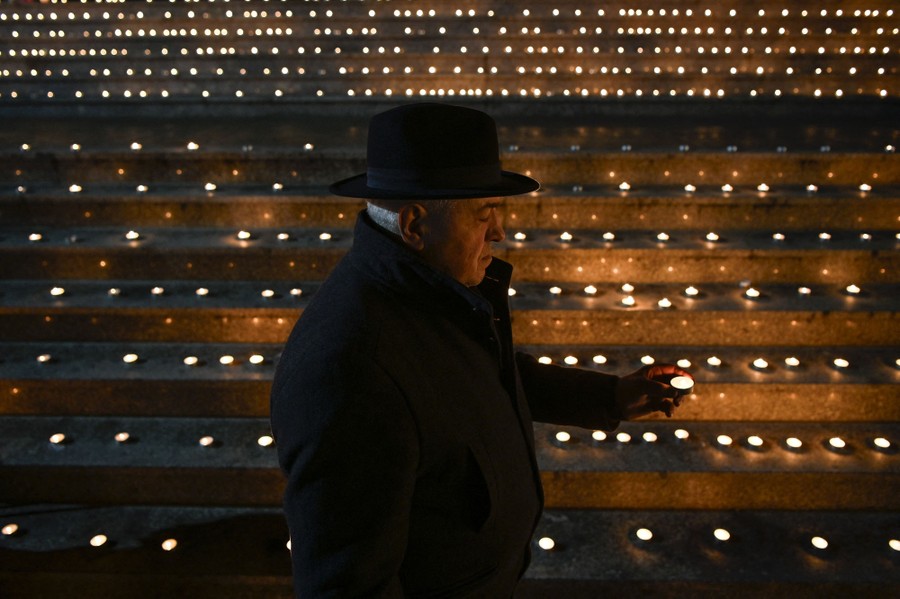 A person lights a candle in front of many other lit candles set on the steps of a theater.