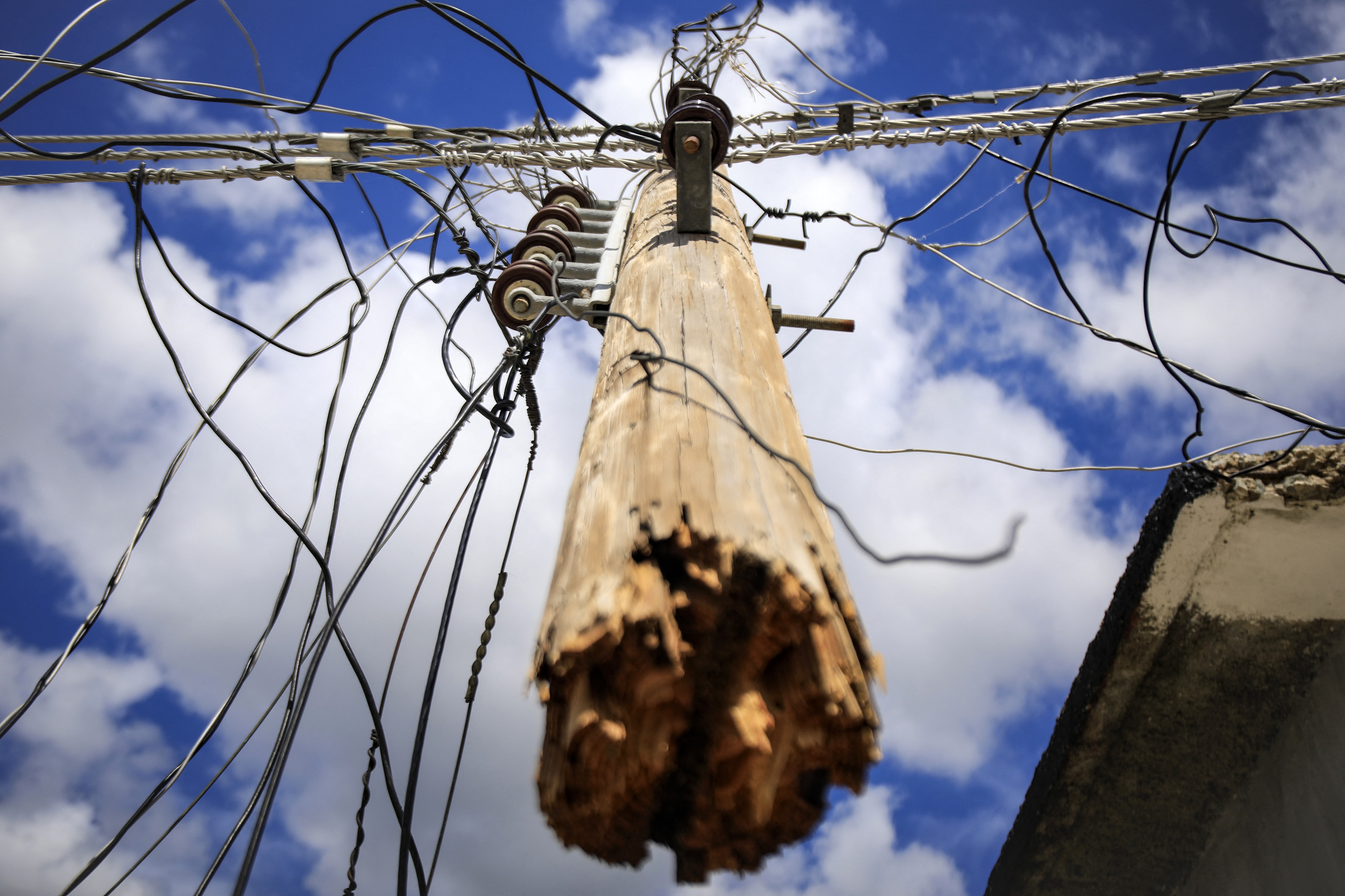 A view looking upward at a utility pole that has been snapped in half by a storm, held up by its wires