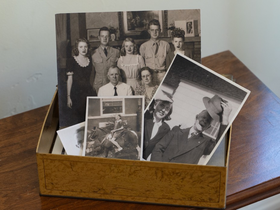 photo of a box of archival black-and-white family photos including a group family shot, a girl on a pony, and a woman standing next to a man in a fedora