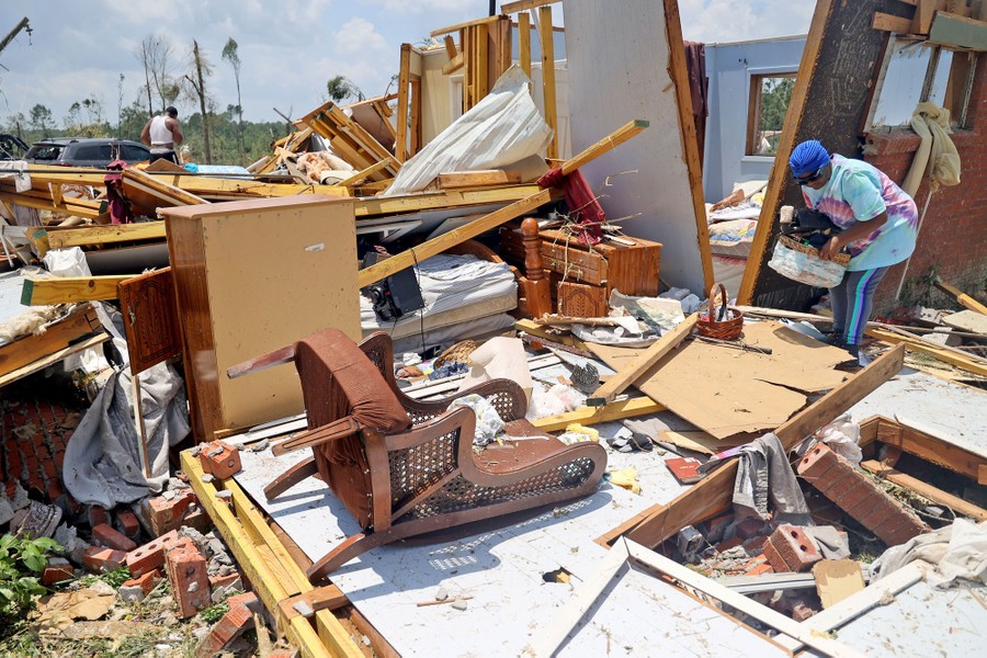 A person gathers belongings from the wreckage of a house destroyed by a tornado.