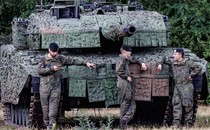 German armed forces stand at ease in front of a battle tank.