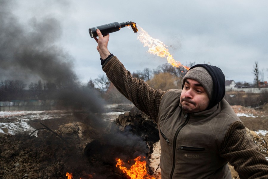 A young man throws a Molotov cocktail in an empty field.