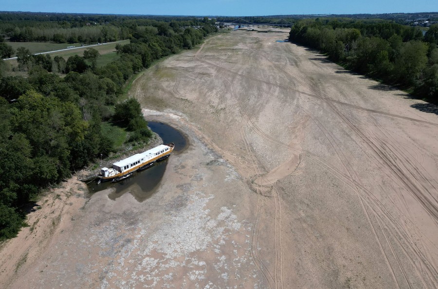An elevated view of a barge sitting in a shallow pond of water along a dried-out riverbed.