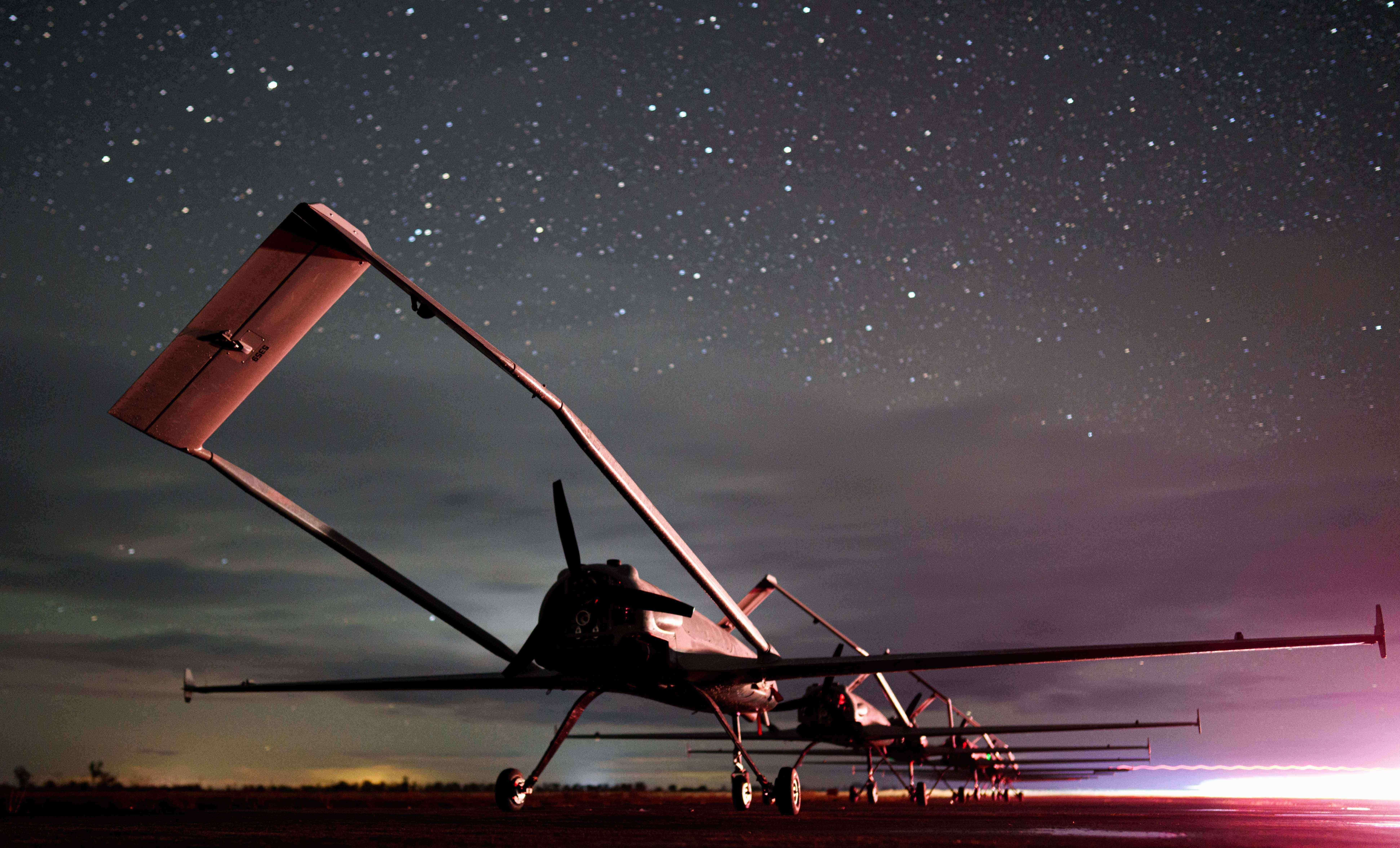 A line of fixed-wing drone aircraft sits on a runway.
