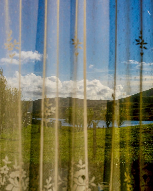 a view of mountains and grass through a curtain
