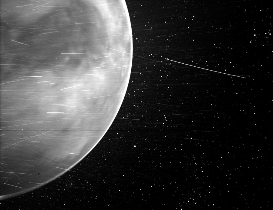 A slightly blurry image of Venus, with numerous light streaks seen in front of the planet and the starry background