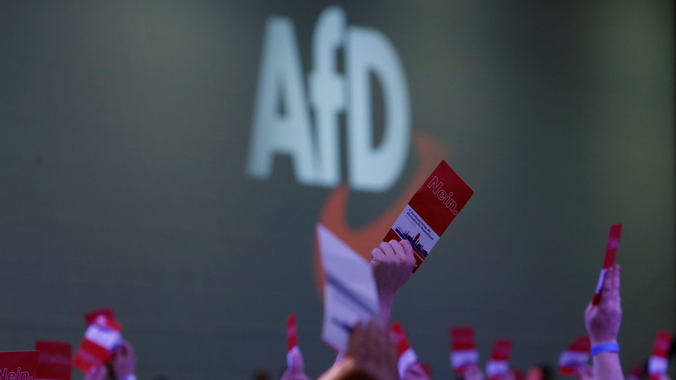 Participants at an Alternative for Germany party congress raise pamphlets in front of a sign reading "AfD."