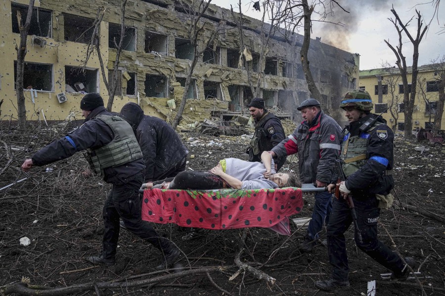 Several emergency workers and volunteers carry a pregnant woman on a stretcher through a debris-strewn courtyard.