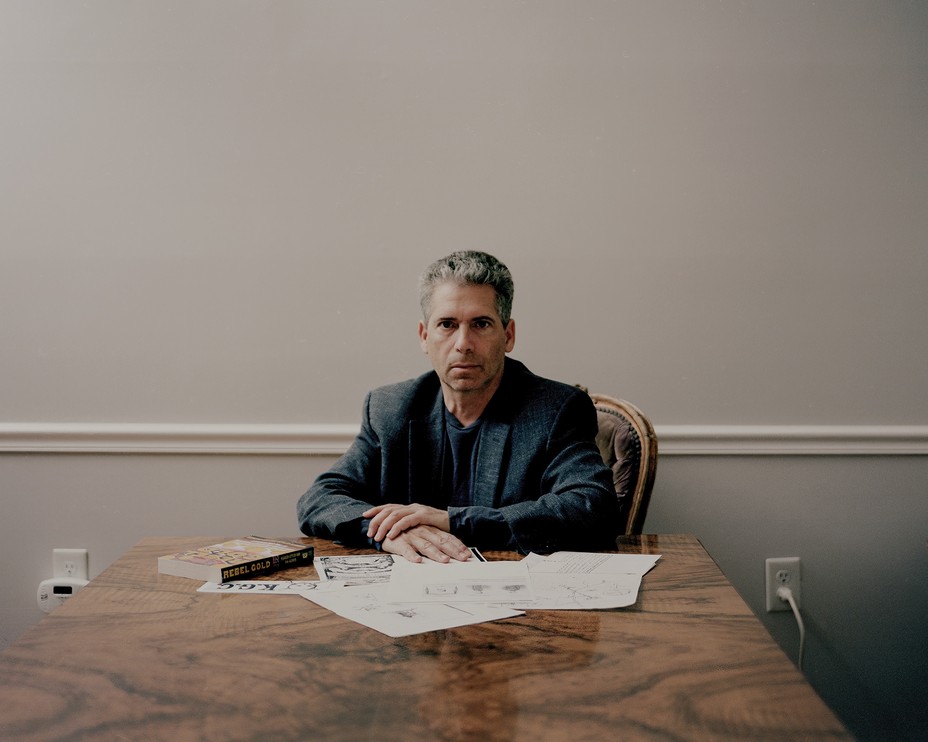 photo of man sitting at large table with hands crossed and papers spread before him